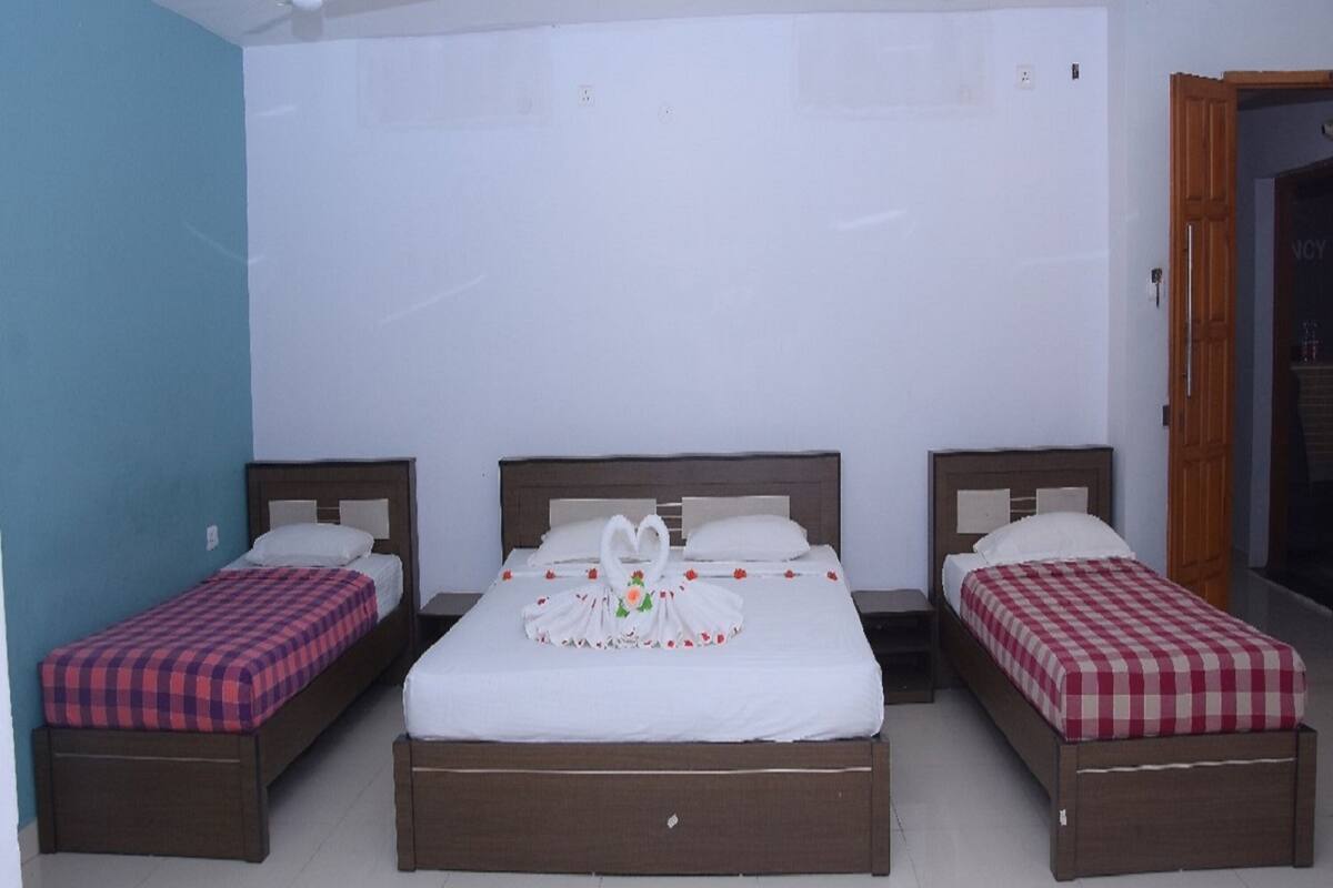 A hotel room with three beds, each with a different checkered bedspread. There are ceiling fans and recessed lighting.