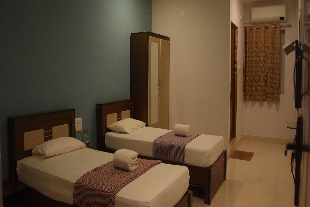 A hotel room with two beds, a wardrobe, a mirror, and a bathroom with a shower curtain.