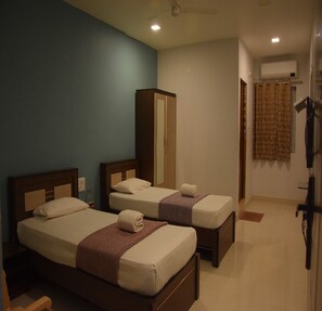 A hotel room with two beds, a wardrobe, a mirror, and a bathroom with a shower curtain. - Mangalam Residency (Kariyapatti)
