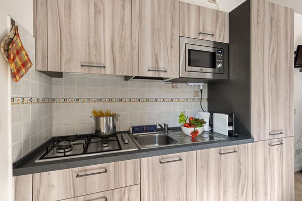 Eine moderne Küche mit Holzschränken, einer Spüle aus Edelstahl, einer Mikrowelle und einem Gasherd.