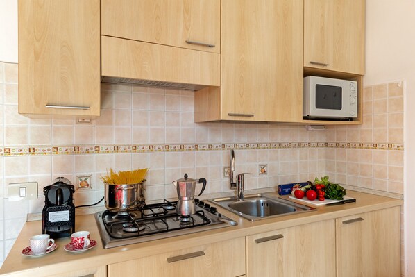 A kitchen with wooden cabinets, a microwave, a stove, a coffee maker, and a sink. - Porto Letizia Como 9, Porlezza, Italy (Porlezza)