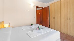 Ein Hotelzimmer mit zwei Betten, einem Holzschrank und einem Nachttisch mit Lampe und Flasche.