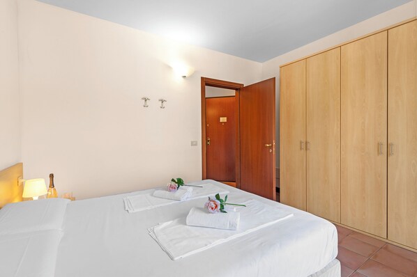 A hotel room with two beds, a wooden wardrobe, and a nightstand with a lamp and a bottle. - Porto Letizia Como 9, Porlezza, Italy (Porlezza)