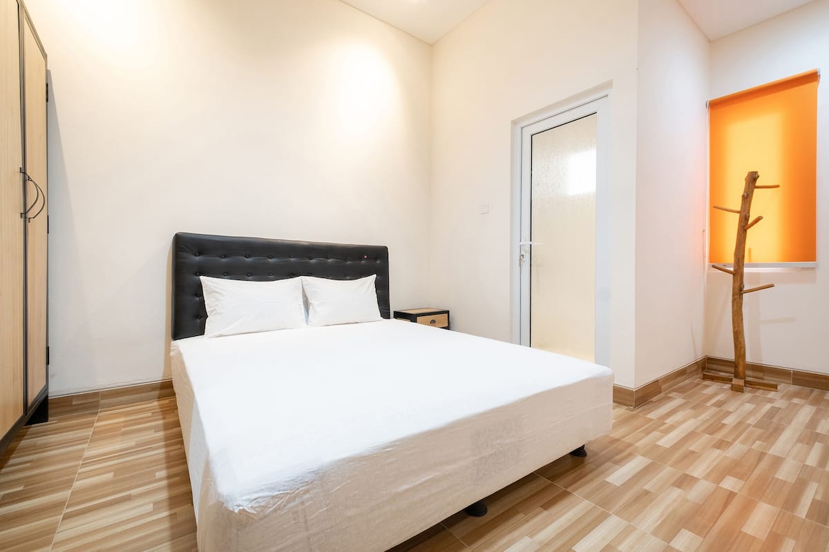 Un dormitorio con cama, mesita de noche, una puerta y una ventana con una escalera de madera.