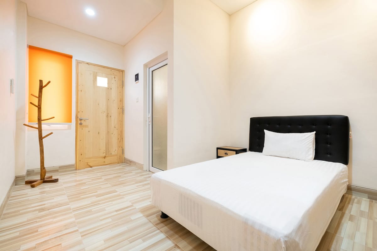 Un dormitorio con cama, suelo de madera, una puerta y una mesita de noche.