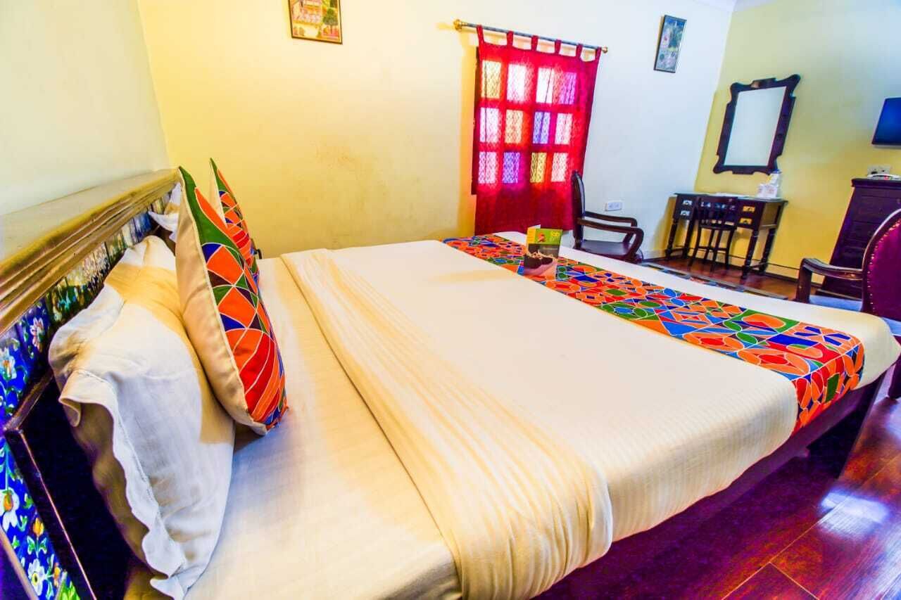 A hotel room with a bed, a desk, a chair, and a window with red curtains.
