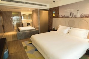 Een hotelkamer met een groot bed, een bureau, een stoel, een klein tafeltje, een prullenbak en een wandlamp.