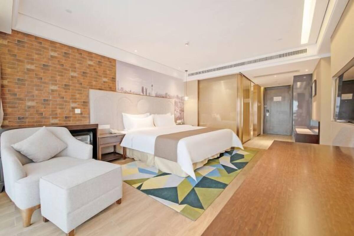 A modern hotel room with a bed, a sofa, a desk, and a TV.