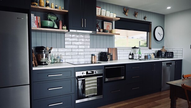 A modern kitchen with dark cabinetry, stainless steel appliances, and a window with a view. - Mount View Accommodation Marrawah (Marrawah)
