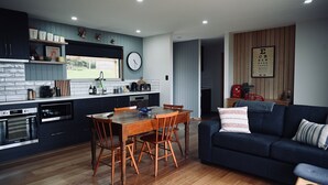 A modern kitchen with dark cabinets, a wooden dining table, and a blue sofa in the living area. - Mount View Accommodation Marrawah (Marrawah)