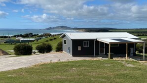 A coastal property with a small house, a covered outdoor area, and a view of the ocean and hills. - Mount View Accommodation Marrawah (Marrawah)