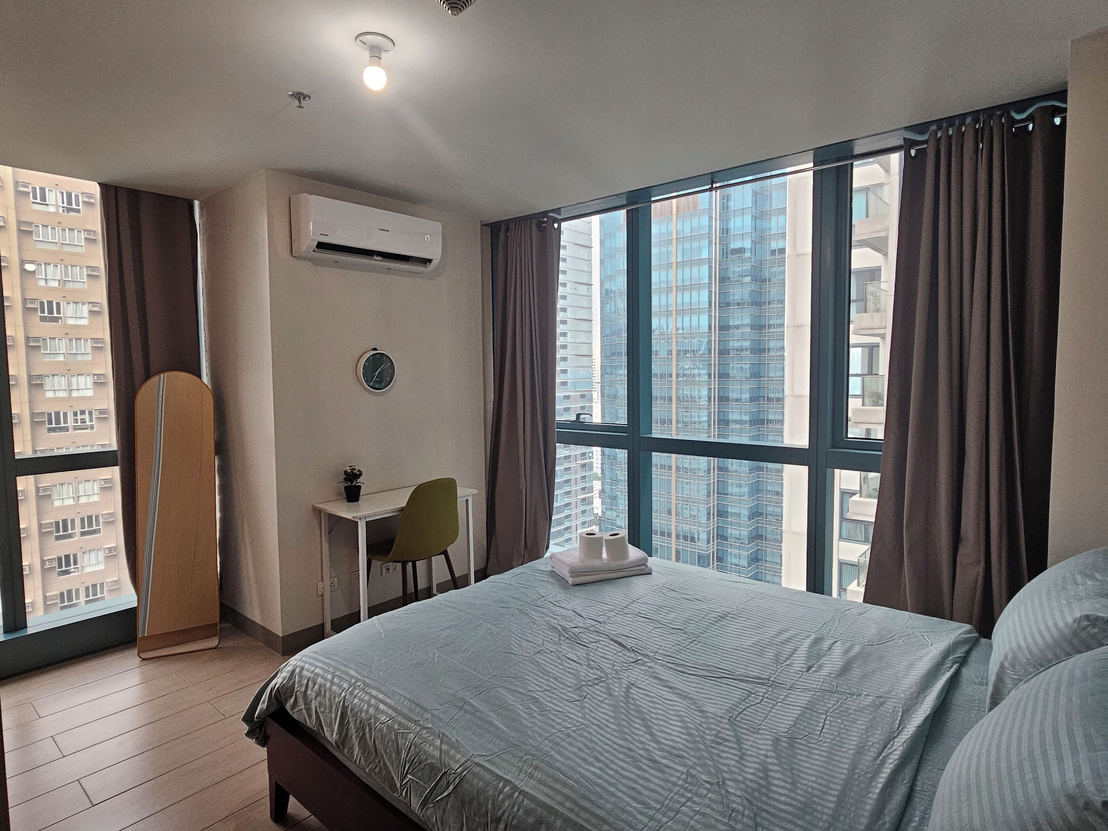 Un dormitorio con una cama grande, un escritorio, una silla, aire acondicionado, un reloj y una ventana con cortinas.