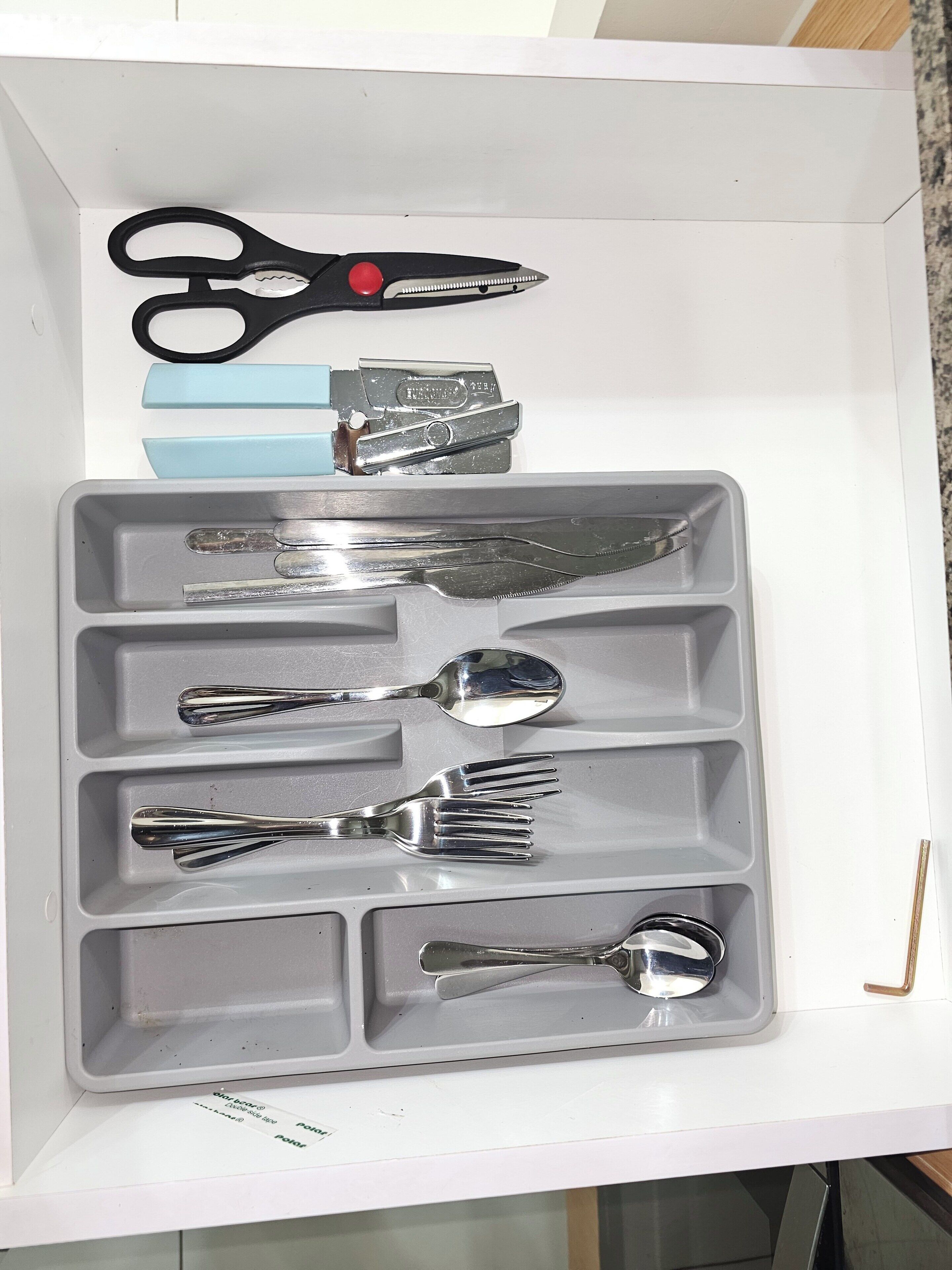 A drawer containing various utensils including a pair of scissors, a knife, a spoon, and a fork.