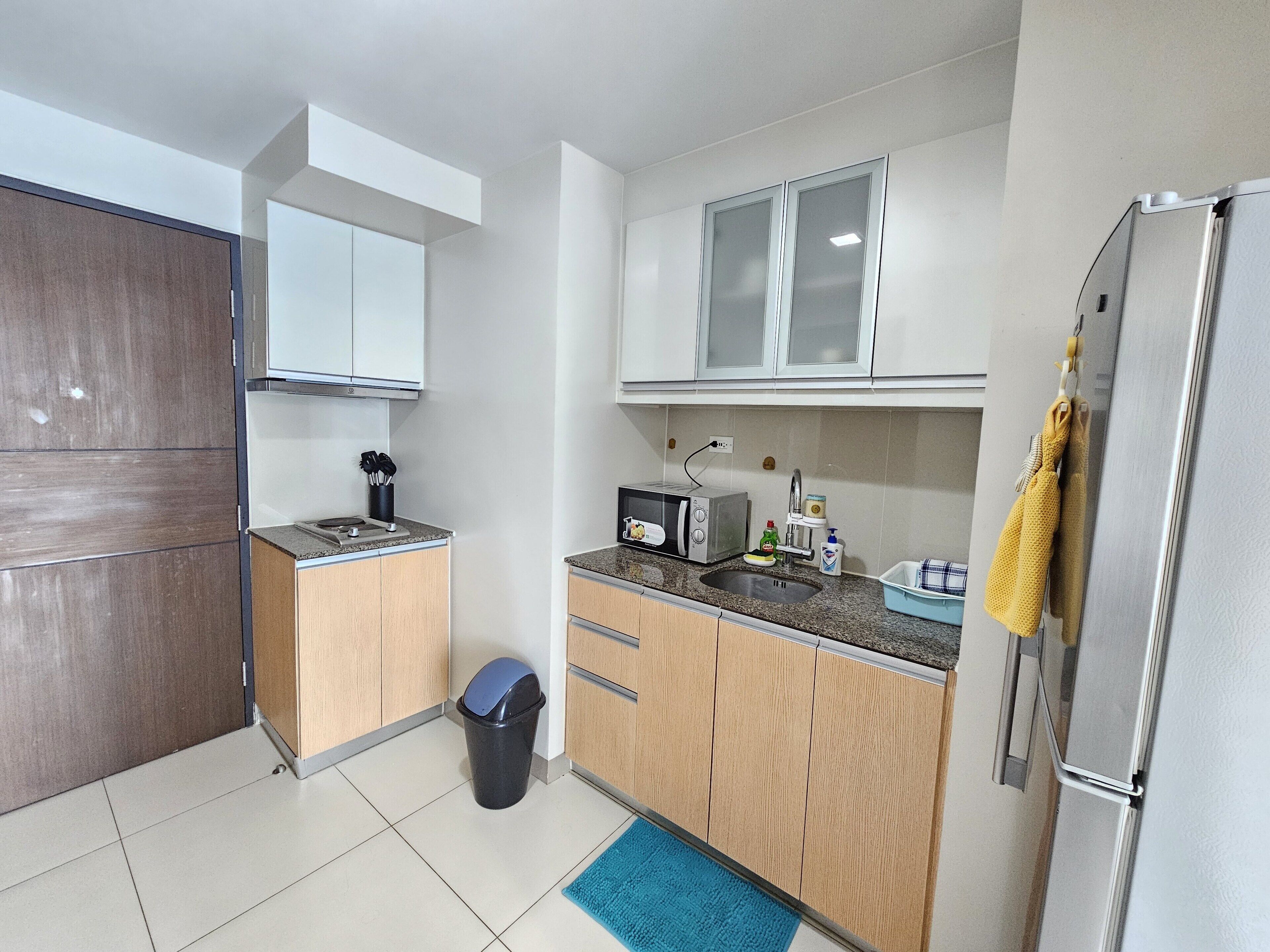 Una cocina compacta con microondas, tostadora, lavabo y un cubo de basura.