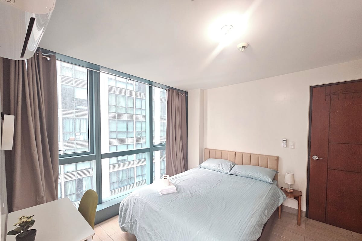 Um quarto com cama, escrivaninha, cadeira, janela e porta.
