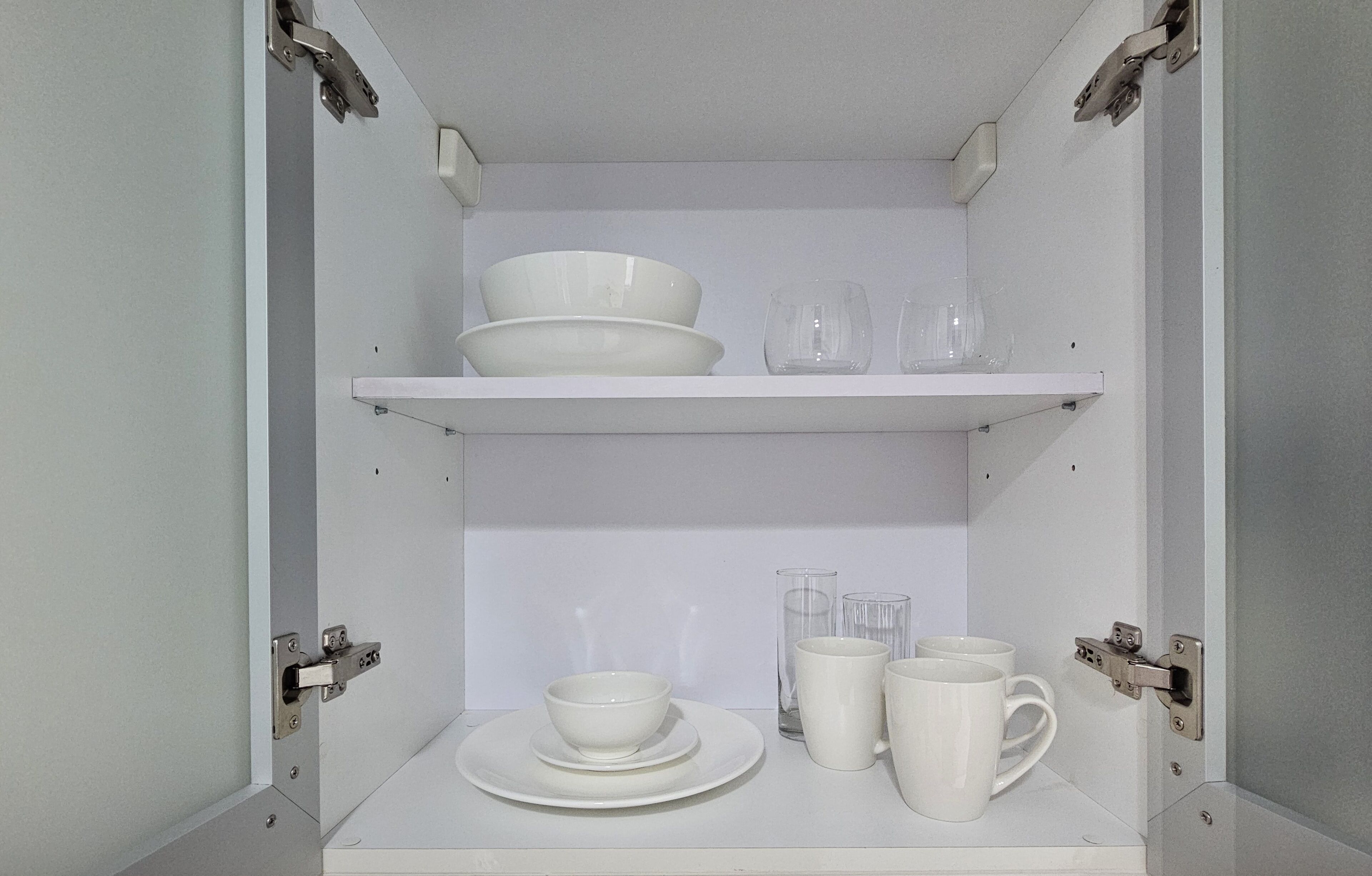 A white cabinet with shelves containing bowls, glasses, and cups.