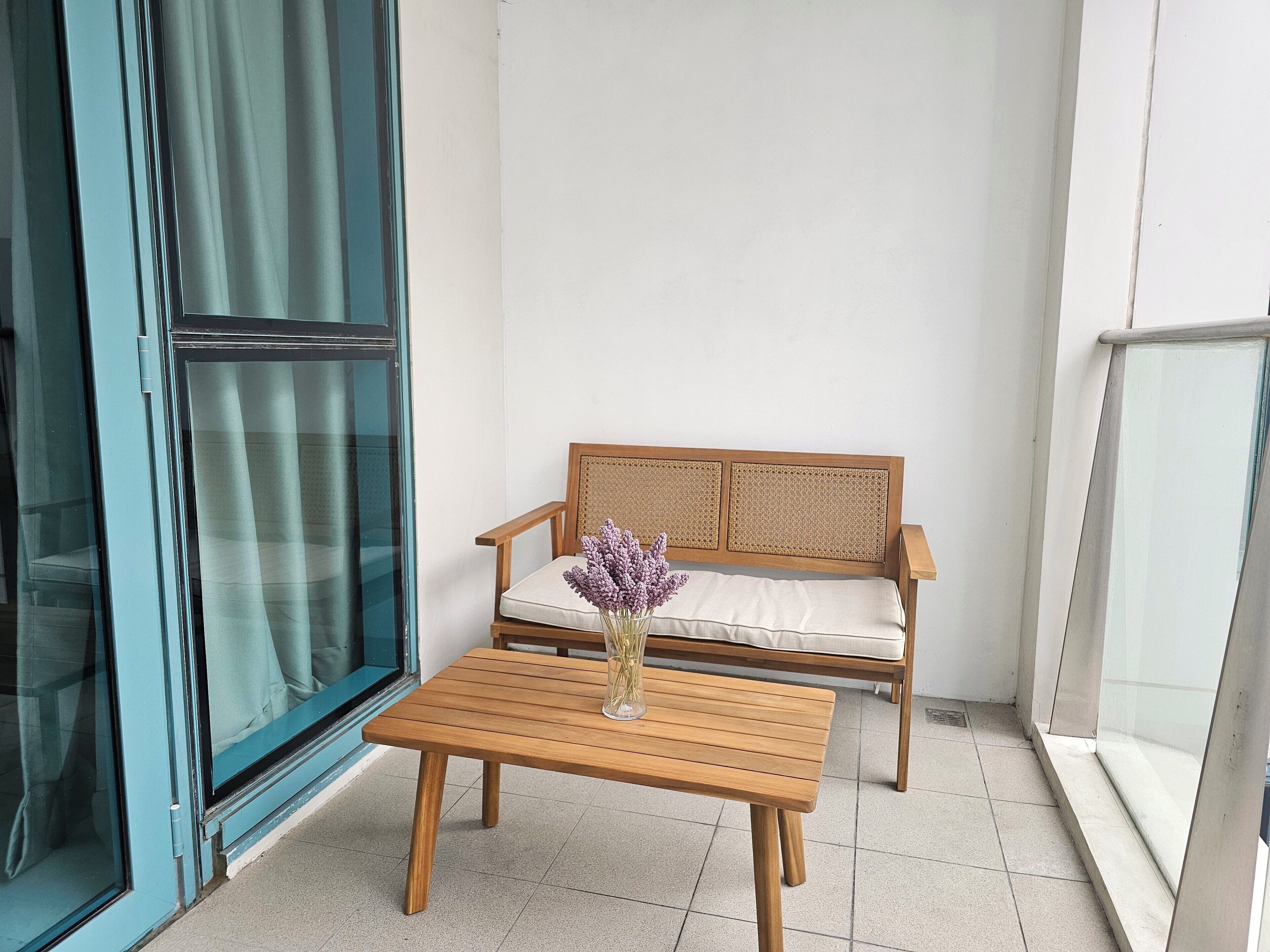 Un balcón con una mesa de madera, un sofá de mimbre y un jarrón con flores.