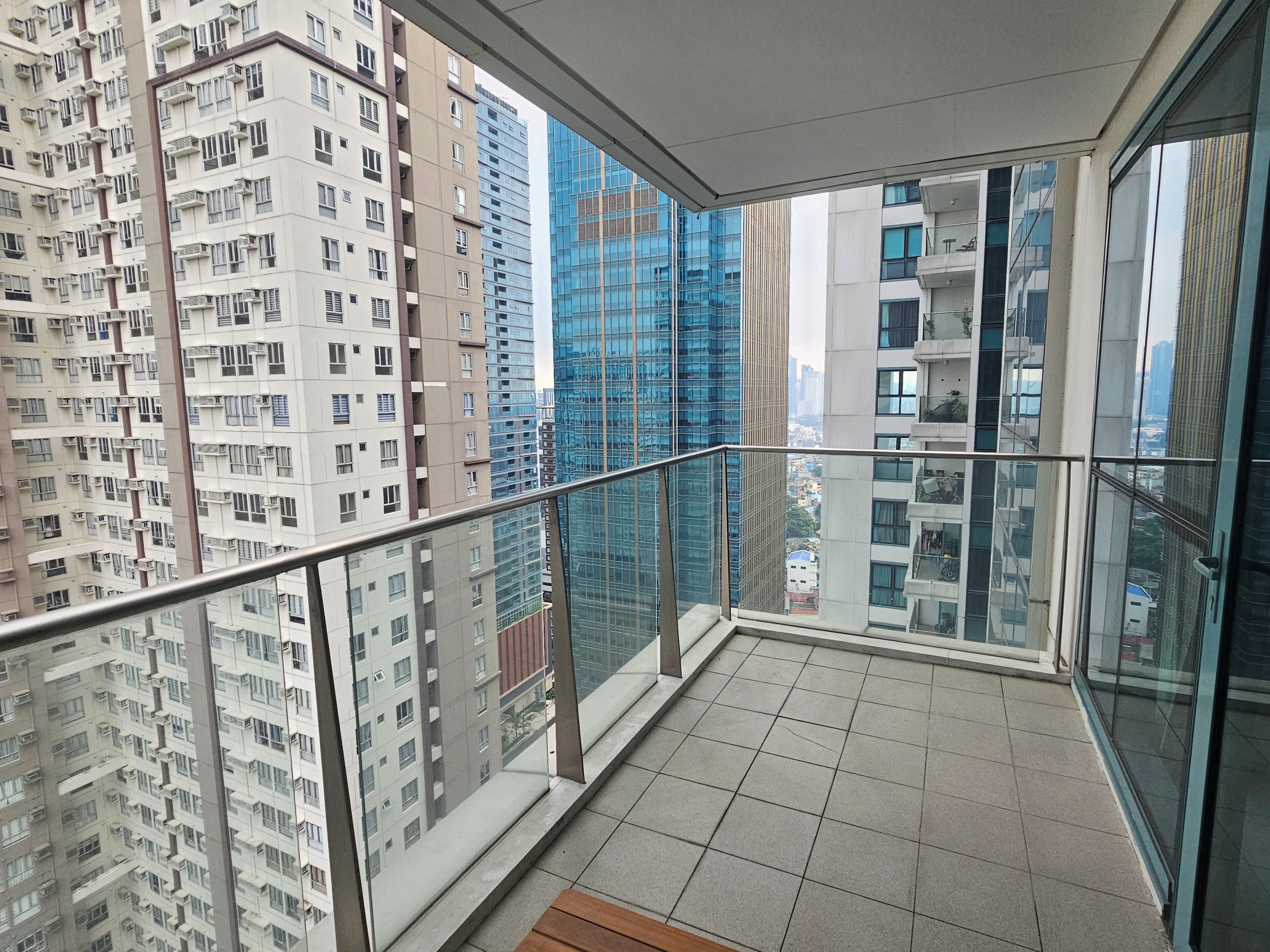 Een balkon met een metalen hekwerk, betegelde vloer en uitzicht op omliggende hoogbouw.