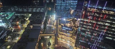 An aerial view of a cityscape at night with illuminated buildings, a prominent shopping mall, and a well-lit intersection.
