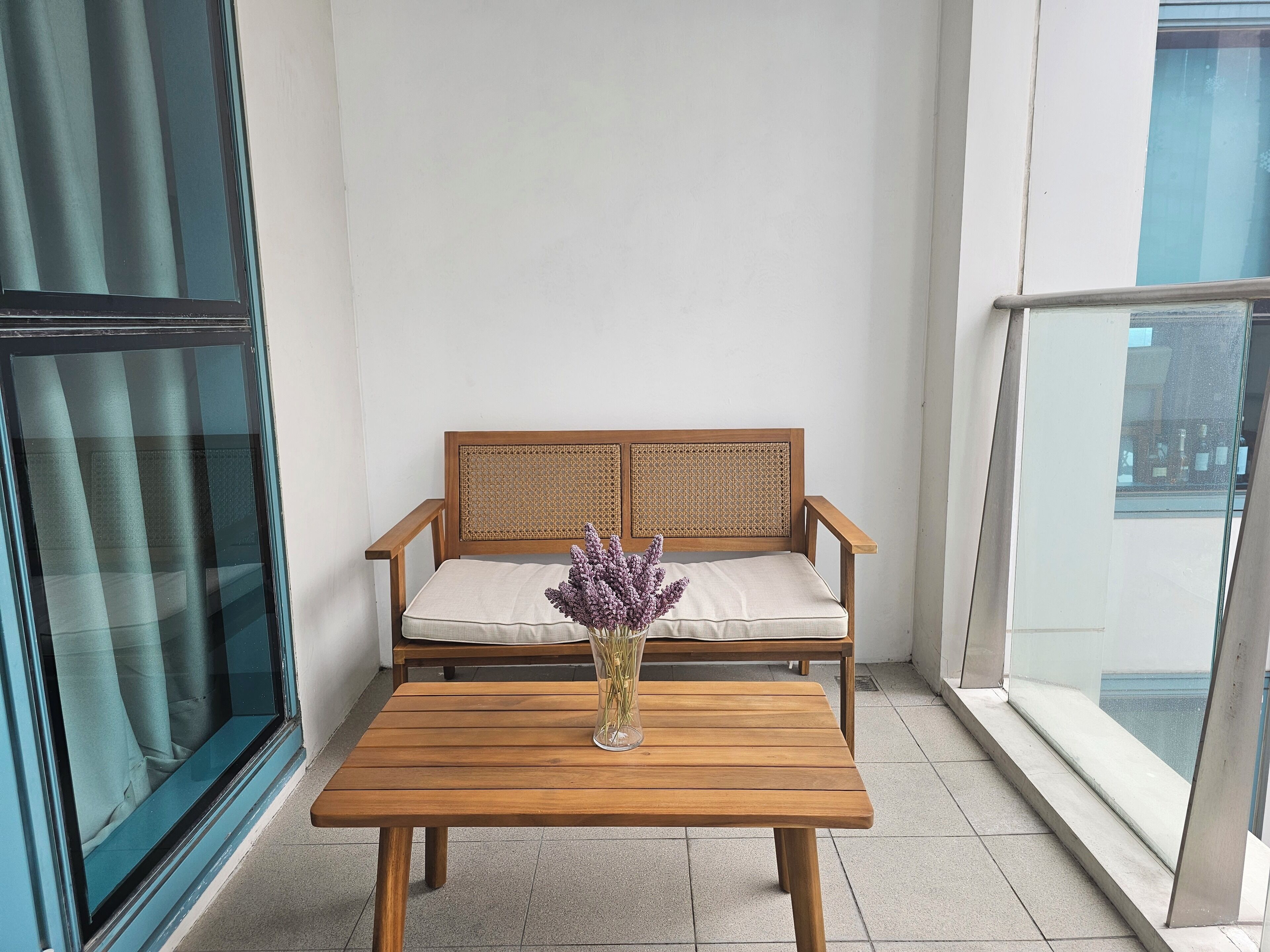 A balcony with a wooden sofa, a small wooden table, and a vase with flowers.