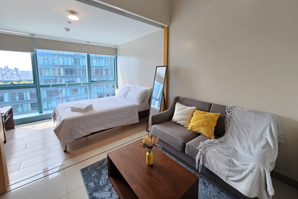 Quarto de hotel moderno com uma grande janela, cama, sofá e mesa de centro.
