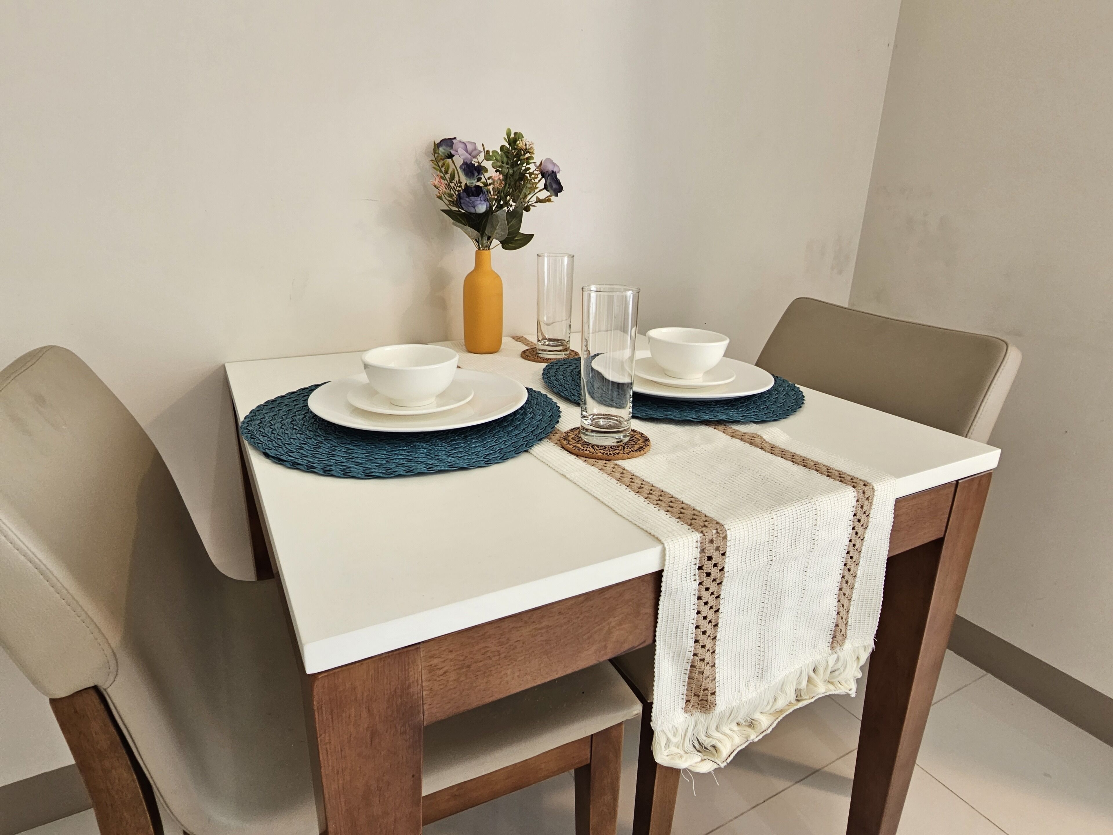 Une table à manger dressée avec de l’assiette blanche, des bols et un verre transparent.