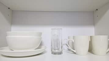 A white shelf with white bowls, a clear glass, and white cups.