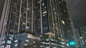 Un immeuble de grande hauteur, doté de nombreux étages et de grandes fenêtres, une rue où circulent des véhicules et des piétons, ainsi que des feux de signalisation.