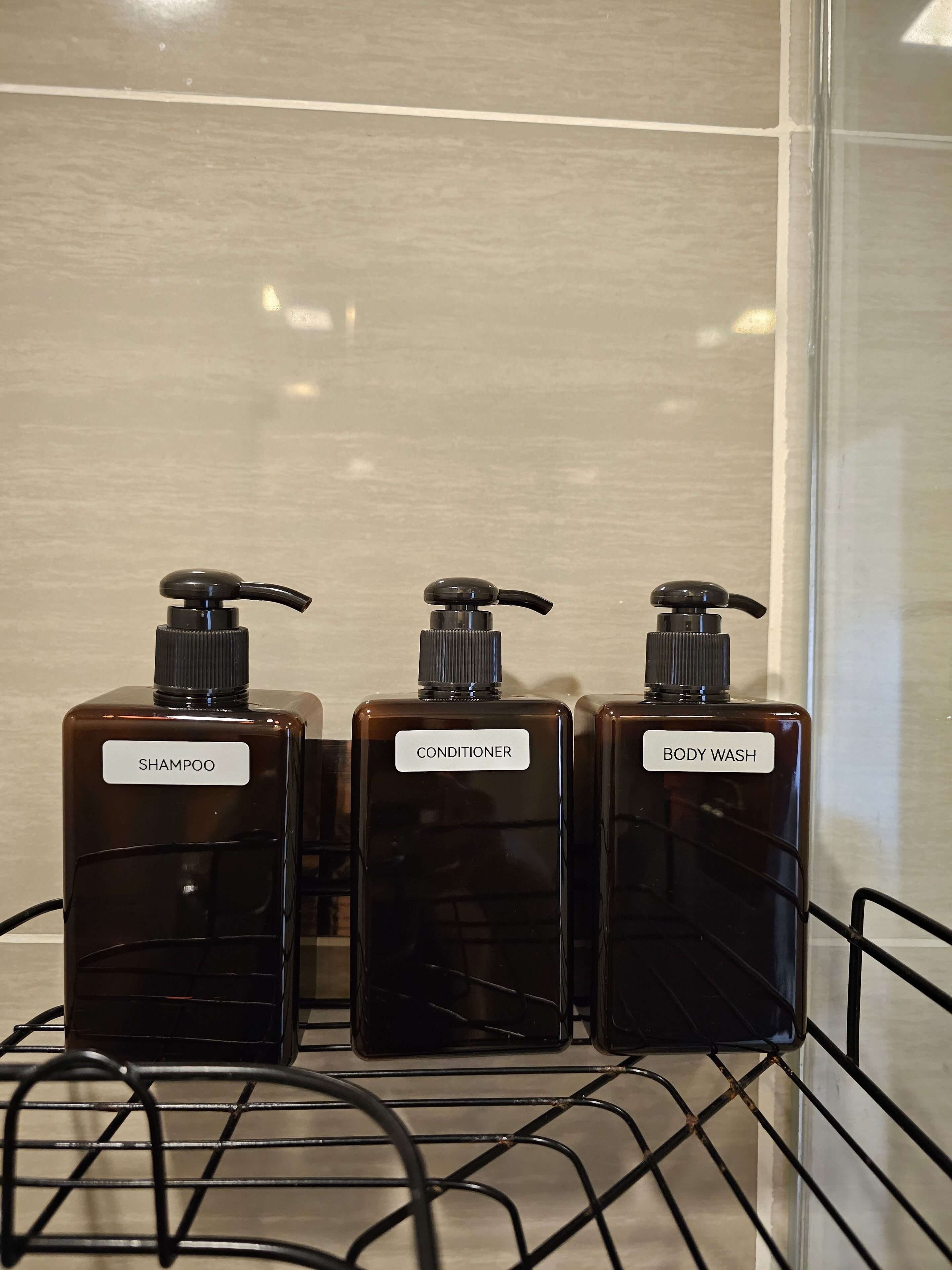 Drei Flaschen Shampoo, Conditioner und Duschgel auf einem Metallregal.