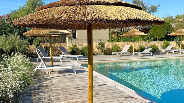 A pool area with thatched umbrellas, lounge chairs, and a wooden deck.