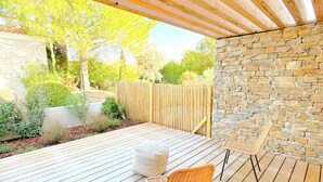 A wooden deck with a stone wall, two wicker chairs, and a white cushion.