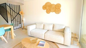A modern living room with a white sofa, a wooden coffee table, and a dining area with a table and chairs.