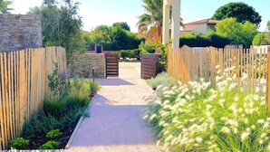 A pathway leading to a gated entrance, flanked by wooden fences and lush greenery.