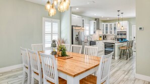 A modern kitchen with white cabinetry, stainless steel appliances, and a wooden dining table with white chairs. - Bougainvillea Beach Bungalow (St. Augustine)