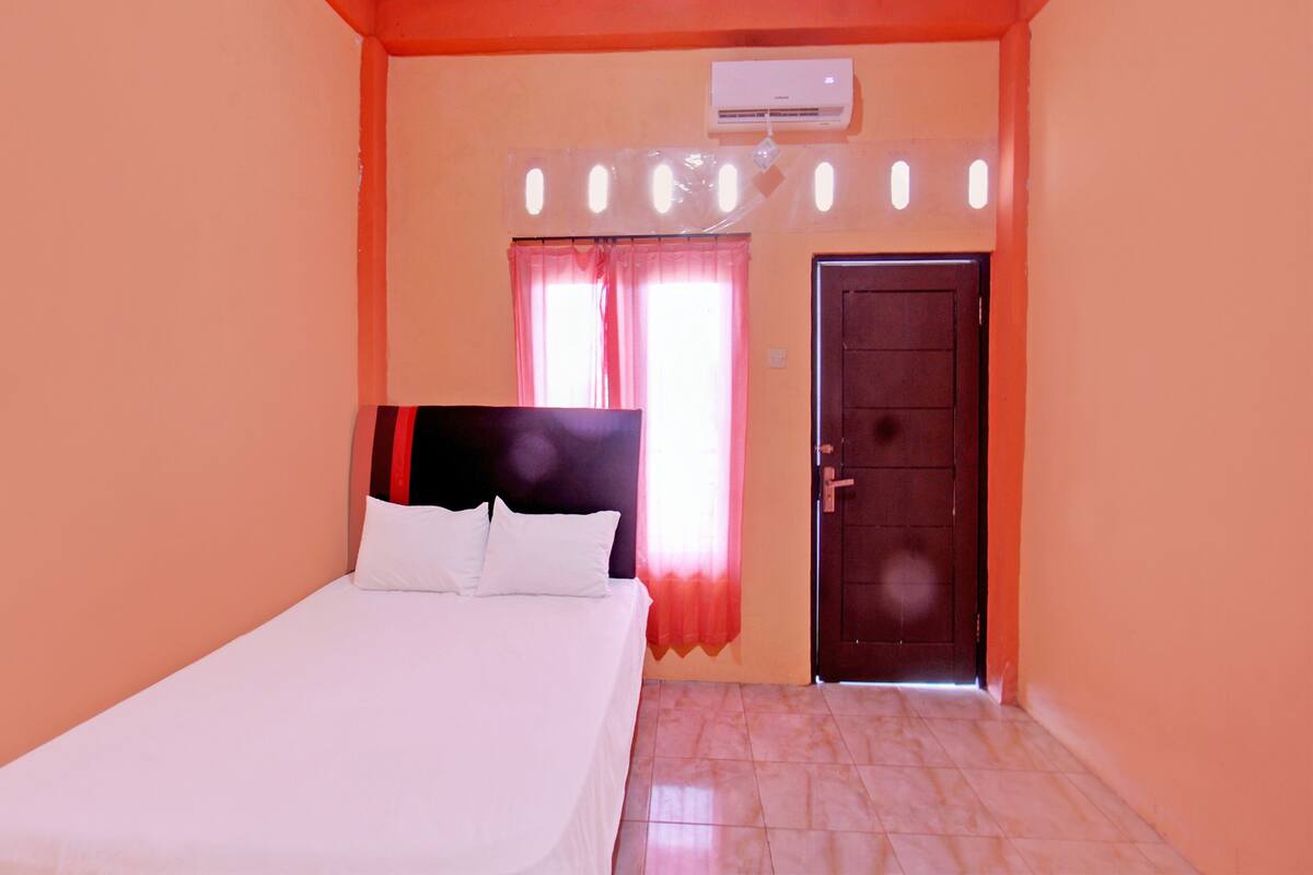 A bedroom with a bed, a window with curtains, an air conditioning unit, and a door.