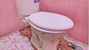 A bathroom with a pink tiled wall and floor, a white toilet, and a metal floor drain. - OYO Life 92847 Penginapan Muslim Walker (Praya)