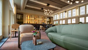 A modern interior with a green sofa, a small table with a vase, and a bar area in the background. - Stadsherberg Ald Weishoès (Venlo)
