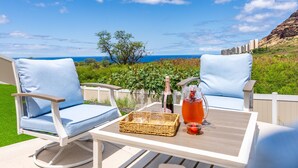 An outdoor seating area with two white chairs and a table, a bottle of champagne, and a glass pitcher with a drink. - Mauna View by AvantStay | 10min to Beach, Backyard (Oahu)