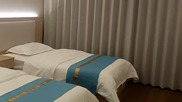 A hotel room with two beds, each with white bedding and blue accents, a wooden nightstand, and a window with vertical blinds. - Qiemo Tazhong Town Moqin Jiayuan Express Hotel (Qiemo)