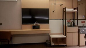 A hotel room with a flat-screen TV mounted on the wall, a wooden desk, a small shelf, a towel rack, a sink, and a mirror. - Qiemo Tazhong Town Moqin Jiayuan Express Hotel (Qiemo)