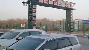 A parking area with multiple cars and a green metal gate with red and white signage. - Qiemo Tazhong Town Moqin Jiayuan Express Hotel (Qiemo)