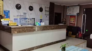 Balcão de recepção com bancada de mármore, relógios e cartazes informativos.