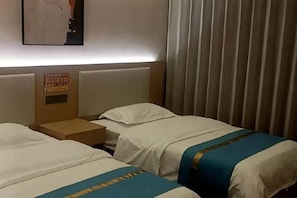 Ein Hotelzimmer mit zwei Betten, einem Nachttisch, einem Schild an der Wand und einem Fenster mit Vorhängen.