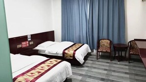 Ein Hotelzimmer mit zwei Betten, einem kleinen Tisch, zwei Stühlen und einem großen Fenster mit blauen Vorhängen.