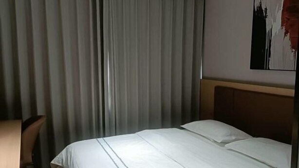 Een hotelkamer met een bed, een bureau en een groot raam met gordijnen.