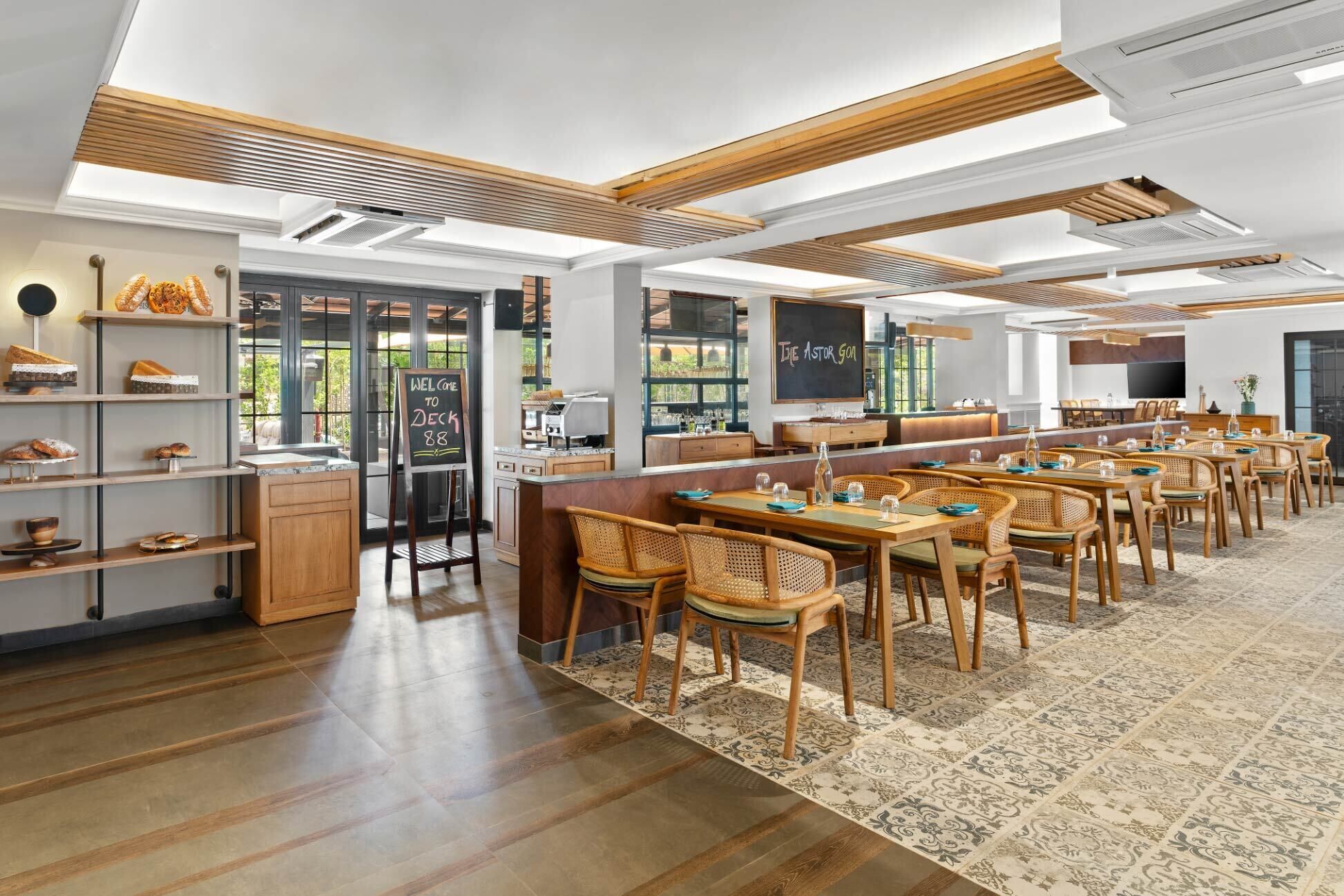 A modern cafe with wooden furniture, a chalkboard menu, and a view of greenery outside.
