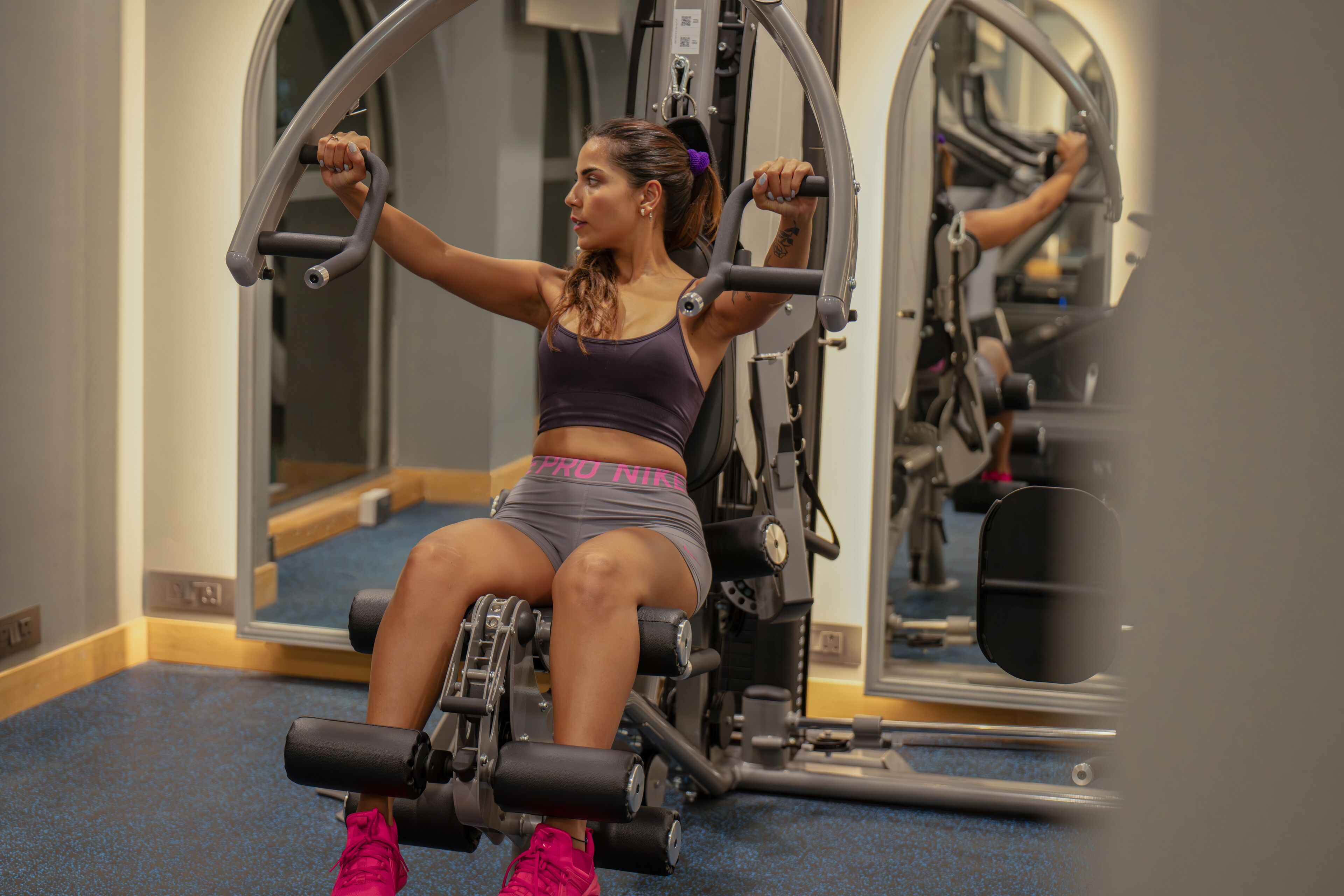 Una persona usando una máquina para piernas en un gimnasio con espejos y otros equipos de ejercicio.