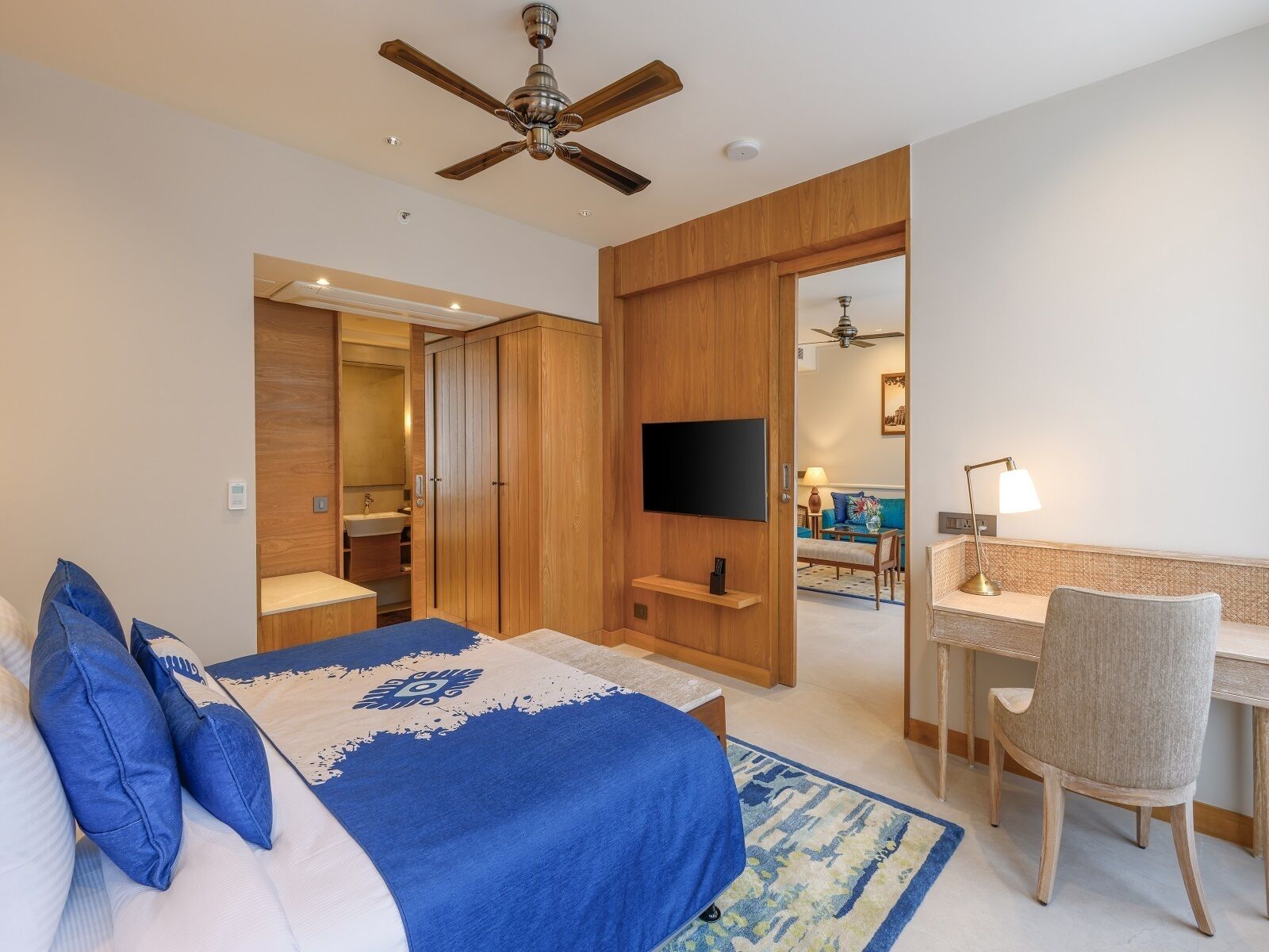 Ein Hotelzimmer mit Bett, Schreibtisch, Stuhl, Fernseher und Deckenventilator.