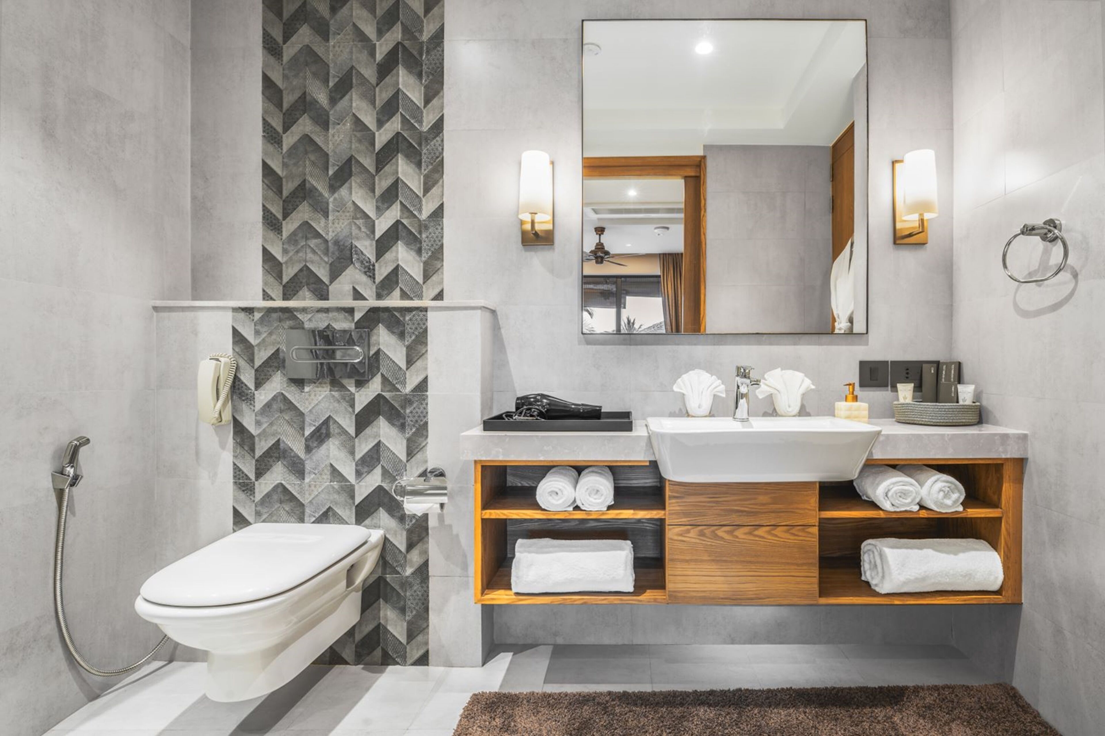 A modern bathroom with a toilet, bidet, and sink. It features a mirror, towel racks, and a shower area.