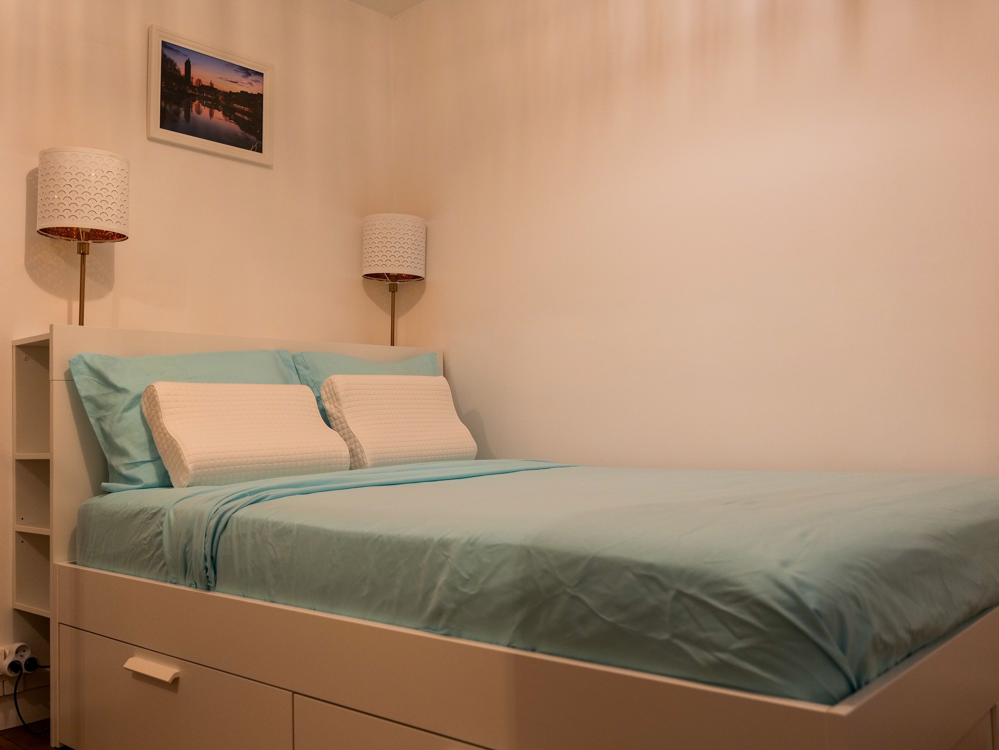 Une chambre à coucher avec un lit, deux lampes de chevet, une table de chevet, un tiroir et un tableau encadré au mur.